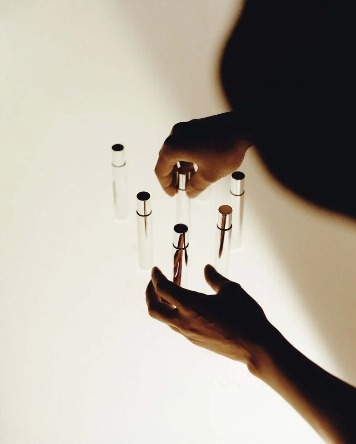 Hands arranging clear glass vials with metallic caps on a white surface, minimal aesthetic
