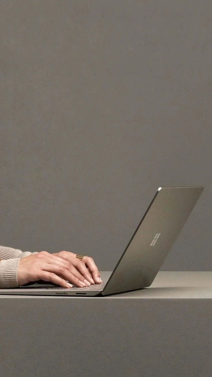 Person typing on a silver laptop on a minimalist grey desk