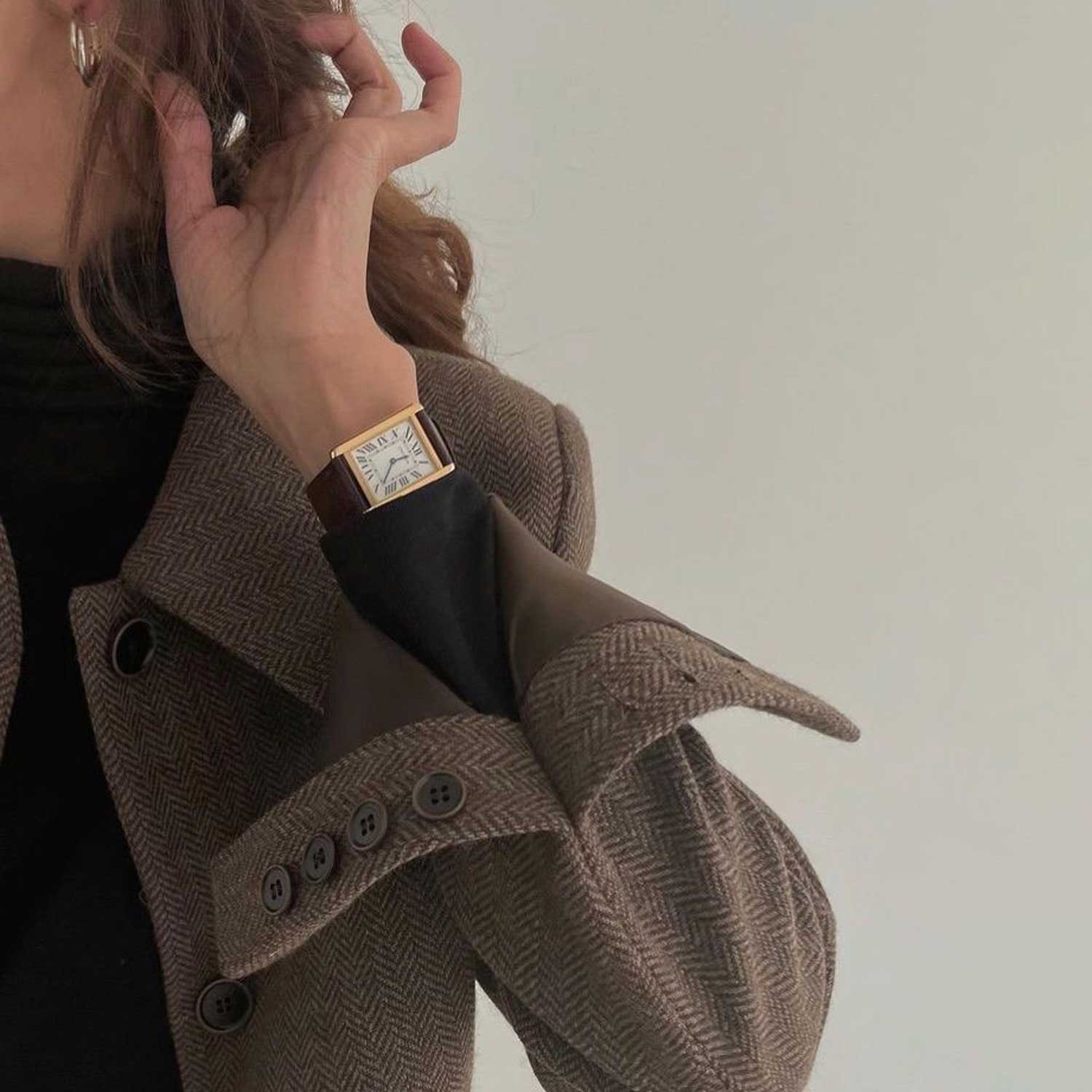 Woman wearing brown herringbone blazer, black turtleneck, and gold rectangular watch