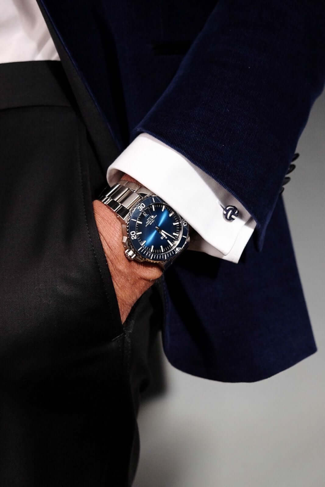 Luxury blue dial wristwatch with metal strap on man in dark suit and white cuff