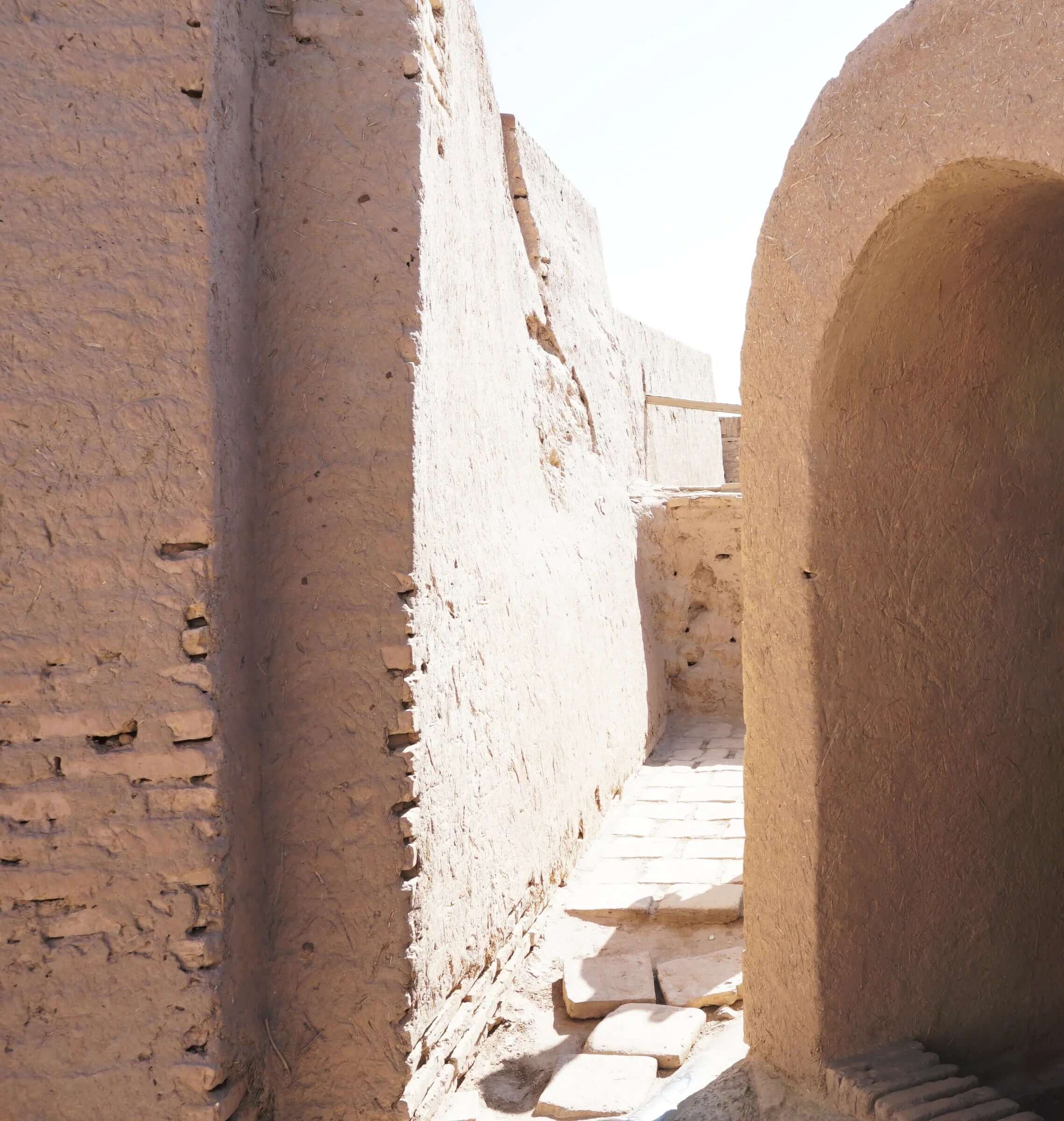Narrow alley with ancient adobe walls and stone pathway in bright sunlight